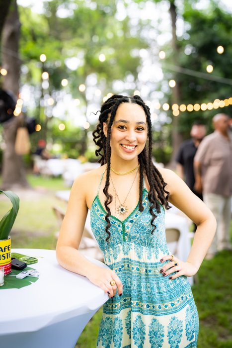 A.G. smiling in a turquoise sundress beside a cocktail table under string lights in the garden